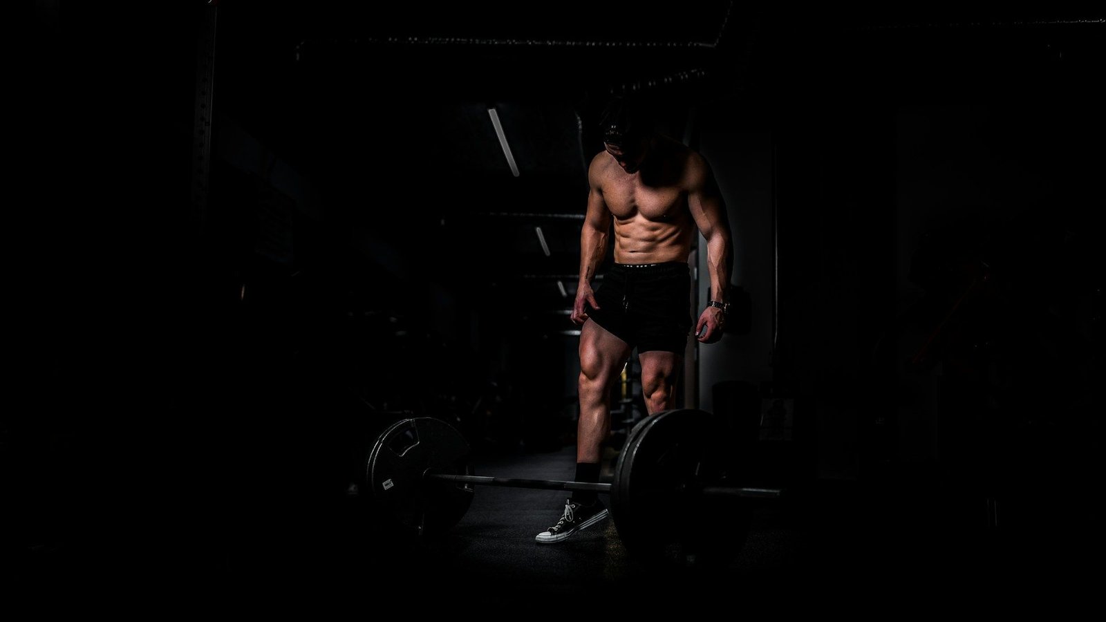 Athlete standing over a loaded barbell in a dimly lit gym
